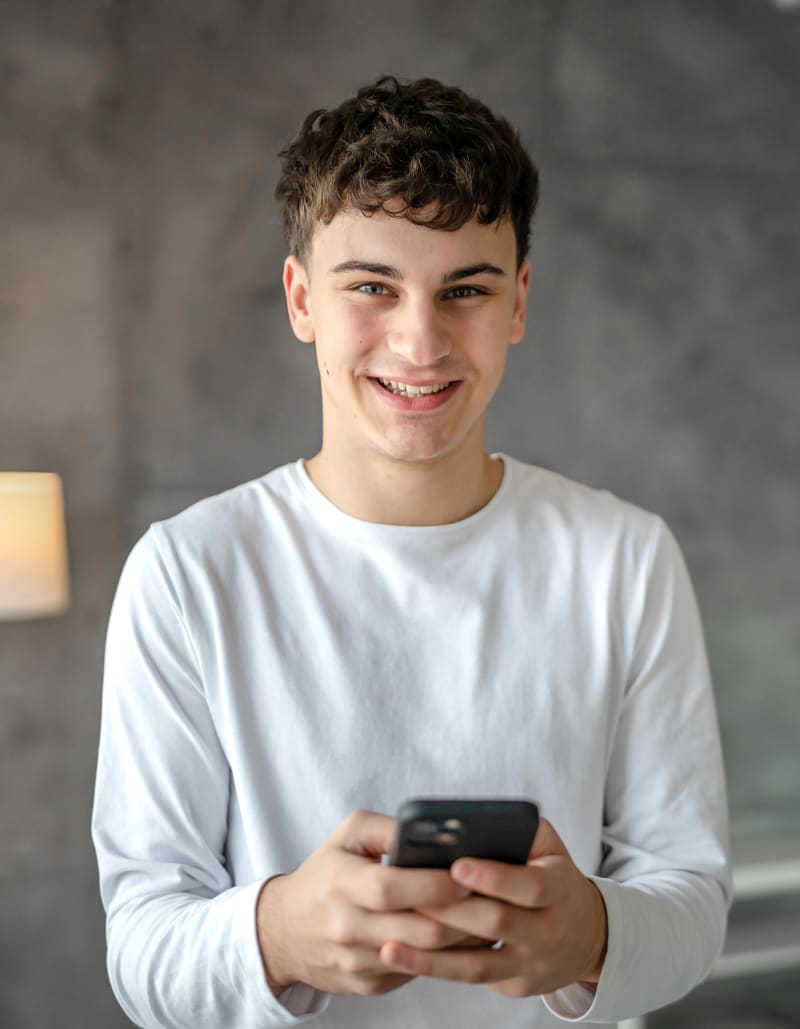 A young teen boy smiling and posing while using his cellphone.